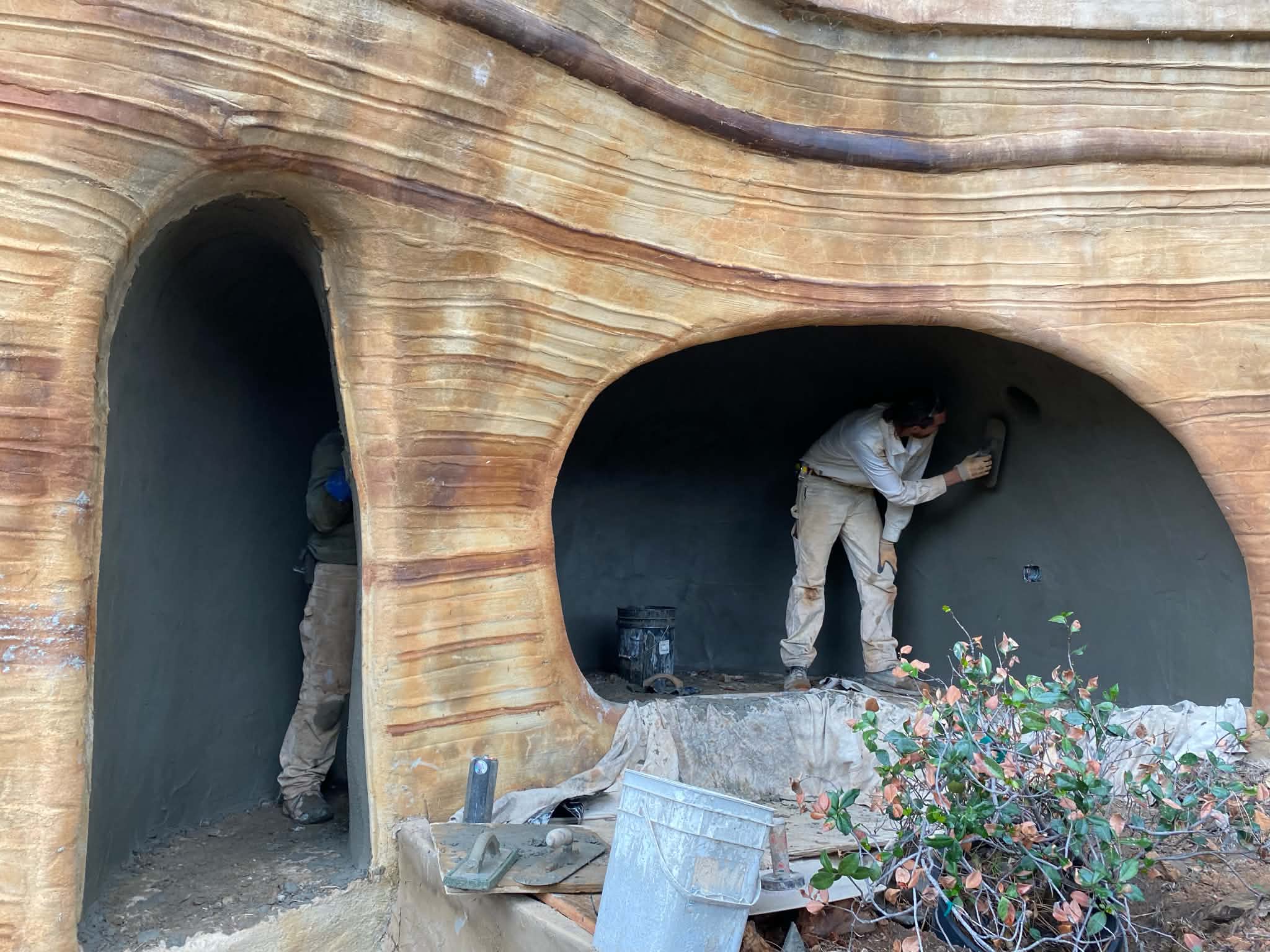 Workers troweling the gray interior of arched alcoves set into a sculpted ferro-cement wall finished to look like banded sandstone